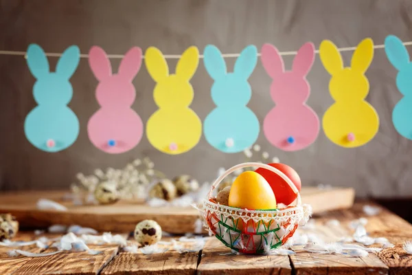 Composição de Páscoa de ovos coloridos de Páscoa na cesta e com guirlanda de coelho no fundo de madeira . — Fotografia de Stock