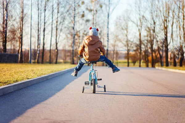 Niño montando su bicicleta en la carretera de asfalto en un día soleado. Vista trasera . — Foto de Stock
