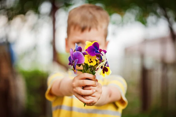 Gyermek kezében tartja a csokor árvácskák virág. Fókuszban a virágok — Stock Fotó