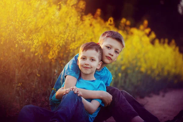 Due simpatici fratelli e sorelle che si abbracciano e si divertono vicino al campo di colza. Amici adorabili insieme nella calda giornata estiva soleggiata. Fratello amore . — Foto Stock