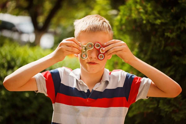 De jongen speelt met fidget hand spinners in zomerdag. Populaire en trendy speelgoed voor kinderen en volwassen. — Stockfoto