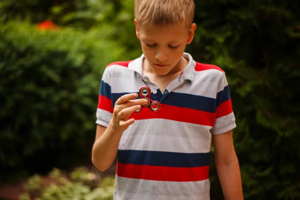 Schoolboy holds a spinner fidget in his hands. Trendy and popular toy for children and adult. — Stock Photo, Image