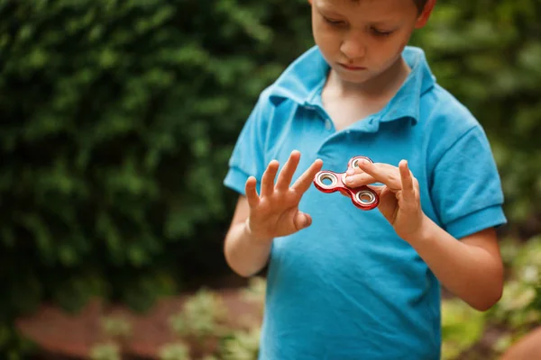 Ładny mały chłopiec bawi się fidget strony tarczy w letni dzień. Popularna i modna zabawka dla dzieci i dorosłych. — Zdjęcie stockowe