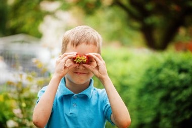 Çocuk holding çilek doğa arka planda onun gözleri önünde gülümseyen portre.