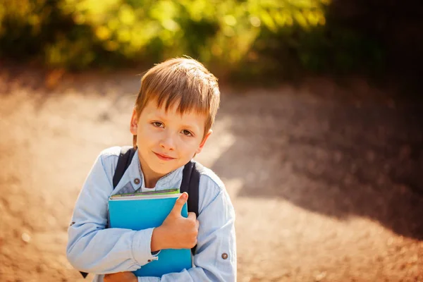 Stående Littleschoolboy med ryggsäck och böcker. Utomhus — Stockfoto