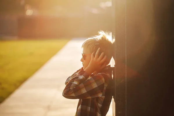 Handsome teenage boy listening to music and using phone on sunset — Stock Photo, Image