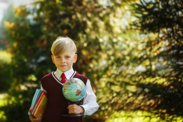 Un ragazzo carino che torna a scuola. Bambino con libri e globo il primo giorno di scuola — Foto Stock