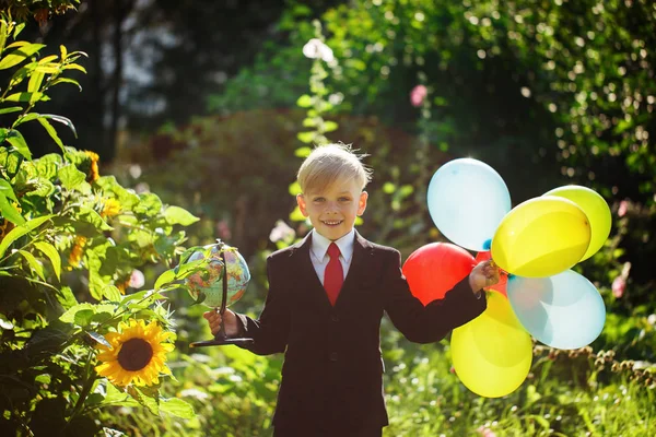 Little boy going back to school. Boy in the suit. Child with globe and colorful balloons on first school day — Stock Photo, Image