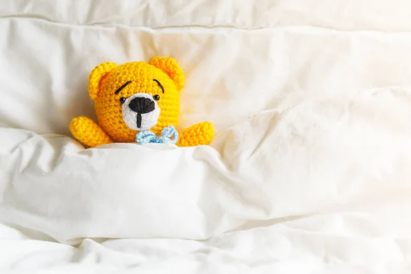 Yellow ill teddy bear lying in bed on white background. — Stock Photo, Image