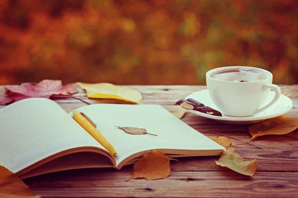Kopje warme thee of koffie met gele bladeren en notitieblok op de achtergrond van de natuur. Concept herfst stemming Rechtenvrije Stockfoto's