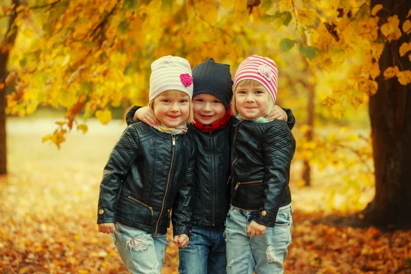 Три счастливых друга дети обнимаются и смеются в осеннем парке — стоковое фото