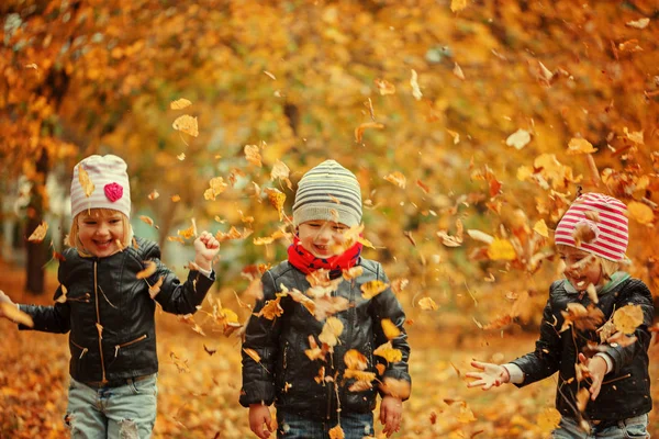 Happy kids having fun with leaves in autumn park — Stock Photo, Image