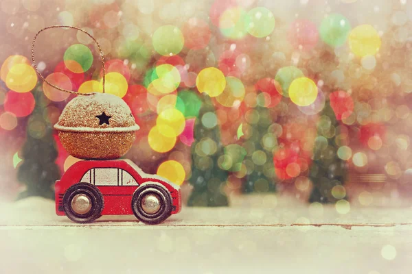 Miniatur-rotes Auto mit einem Geschenk auf dem Dach auf buntem Bokeh-Hintergrund. — Stockfoto