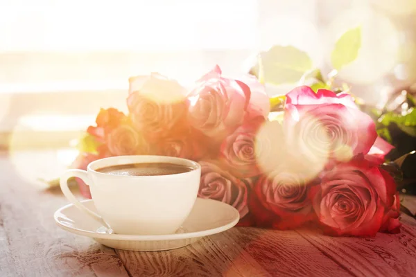 Filiżankę kawy i bukiet różowe róże na stole — Zdjęcie stockowe