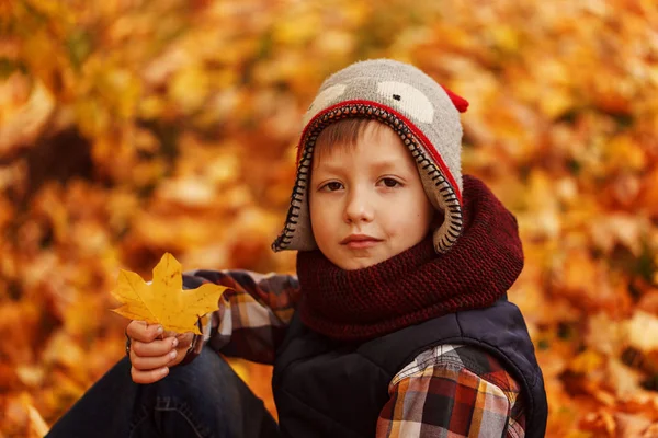 Cute little boy infunny hat and warm scarf at golden autumn in park. — Stock Photo, Image