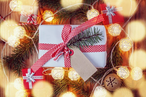 Caja de regalo de Navidad sobre fondo de madera con ramas de abeto, campana de jingle, pequeños regalos y luz de Navidad. Navidad y Feliz Año Nuevo composición. Vista superior . — Foto de Stock