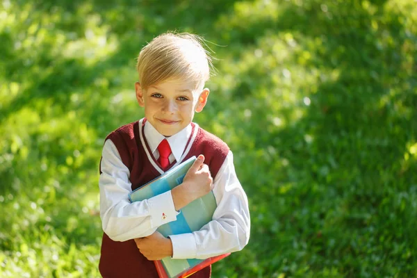 Retrato pequeño colegial sobre fondo de la naturaleza. Niño con libros y uniforme vestido. Educación para niños. Regreso al concepto escolar . —  Fotos de Stock