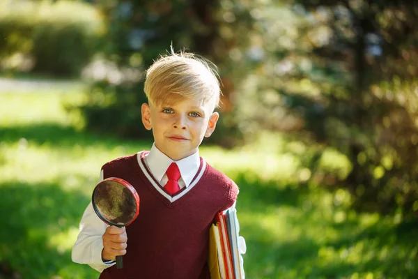 Portrait little schoolboy on nature background. Child with books and loupe. Education for kids. Back to school concept — Stock Photo, Image