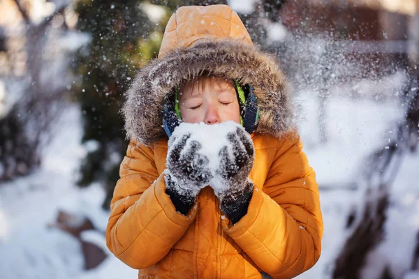 Menino bonito, soprando flocos de neve lá fora no dia de inverno . — Fotografia de Stock