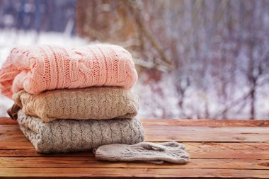Stack of knitted clothes on wooden tableon winter nature background. clipart