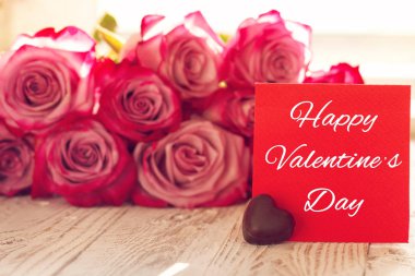 Sevgililer için boş kırmızı kağıt kartıyla dackground üzerinde pembe güller.