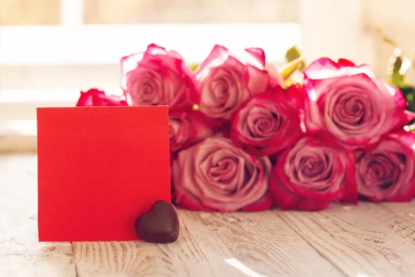 Чистая красная бумажная карточка с шоколадом на день святого Валентина или матери или женщины. Фон с розовыми розами — стоковое фото