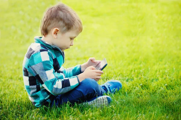 タブレットを持った少年が草の上に座る — ストック写真