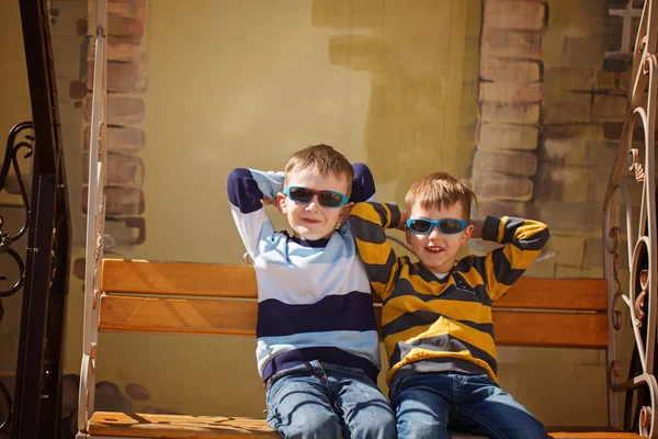 Маленькие мальчики в солнечных очках катаются на качелях. Концепция дружбы — стоковое фото
