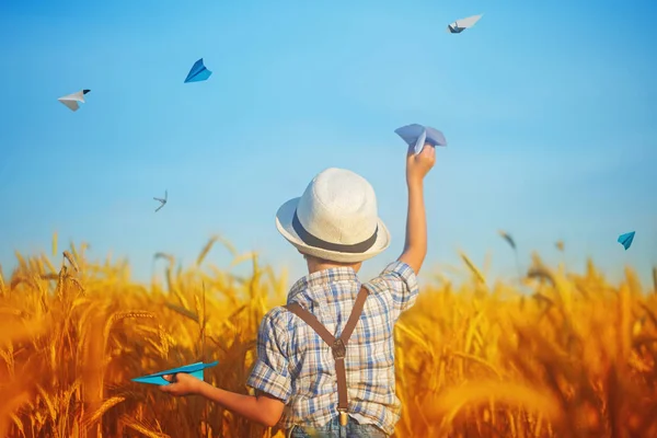 Cute child holding in hand paper airplane in the wheat golden field on a sunny summer day. — Stock Photo, Image