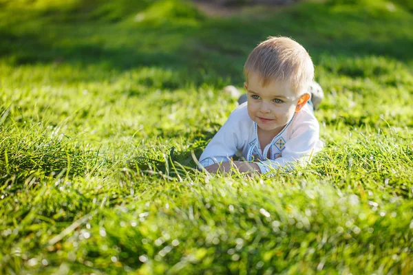 Piccolo ragazzo biondo sdraiato sull'erba verde nella soleggiata giornata estiva . — Foto Stock