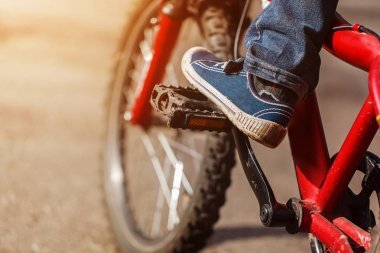 Çocuk bisikletçi ayak üzerinde Bisiklete binmek detay güneşli yolu açık. Closeup pedal ve ayak