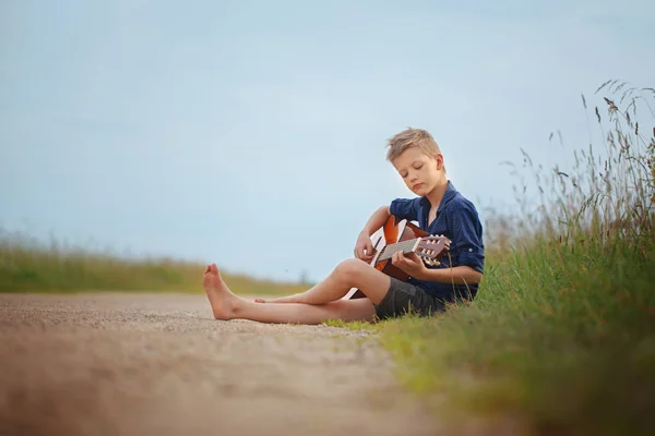 Schöner netter Junge spielt an einem Sommertag auf einer Akustikgitarre. — Stockfoto