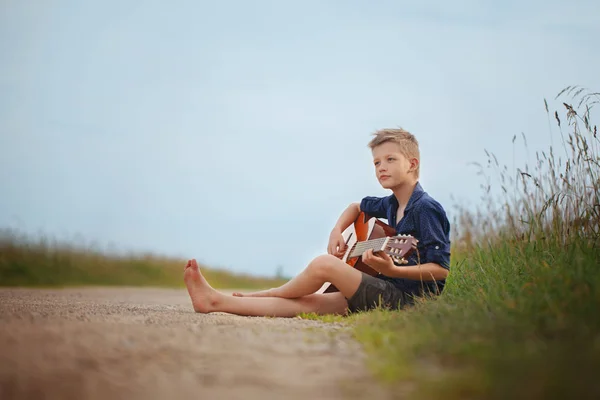 Schöner netter Junge spielt an einem Sommertag auf einer Akustikgitarre. — Stockfoto