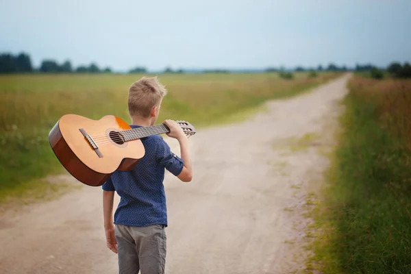 Stilig pojke med gitarr gå på vägen i sommardag. Bakifrån — Stockfoto