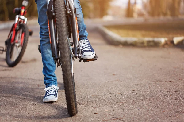 Criança em uma bicicleta na estrada de asfalto no dia de primavera ensolarado. Fechar o pedal e o pé — Fotografia de Stock