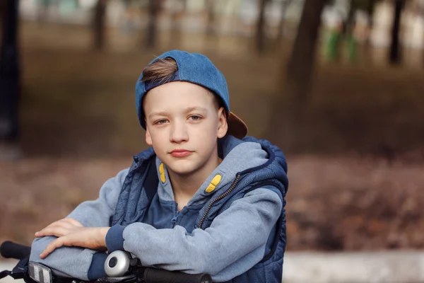 Portret knappe jongen op een fiets op asfaltweg in het voorjaar park. — Stockfoto