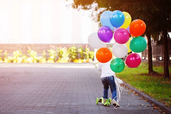 Mutlu çocuk balon dışında bir sürü oyun ve bir scooter sürme. Arkadan Görünüm