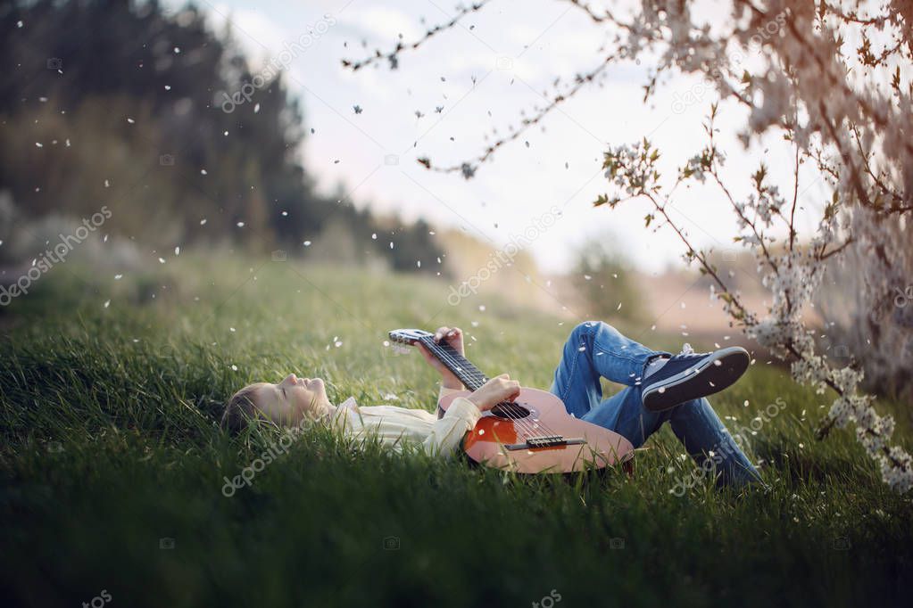 Cute boy lies on the grass with a guitar on sunset.