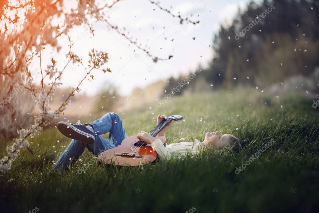 Cute boy lies on the grass with a guitar on sunset.