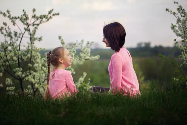 小さな女の子と彼女の母親を夏の日に草の上に座って。バックからの眺め. — ストック写真