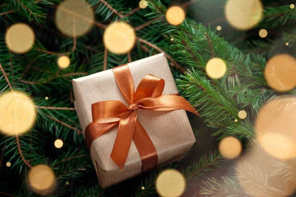 Різдвяний подарунок або подарункова коробка, загорнуті ремесла на фоні ялинових гілок зі світлою блискучою гірляндою . — стокове фото
