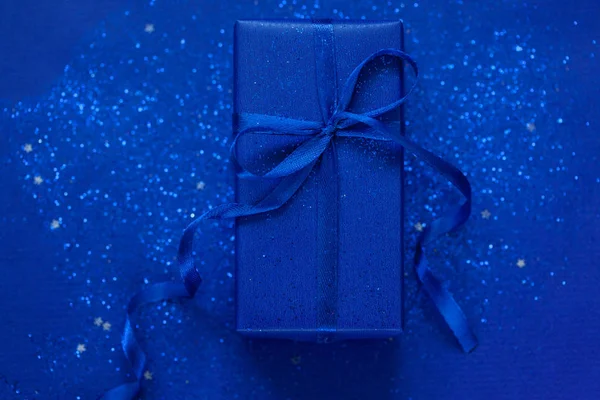 Caja regalo o regalo azul con purpurina azul y confeti plateado en forma de estrella sobre fondo azul. Concepto festivo . — Foto de Stock