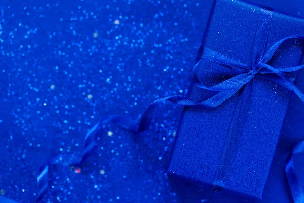 Синя подарункова коробка з синім бантом на модному синьому фоні з маленькими блискітками. Стиль плоского шару . — стокове фото