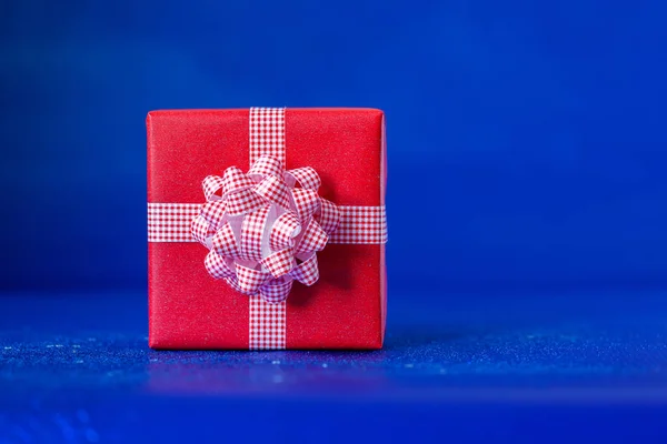Rode geschenkdoos met grote strik op blauwe achtergrond. Feestelijk concept. — Stockfoto