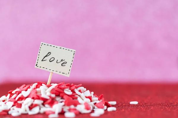 Tekst miłosny skomponowany na pokładzie w stercie czerwono-białych serc na różowym tle. Koncepcja Walentynki — Zdjęcie stockowe
