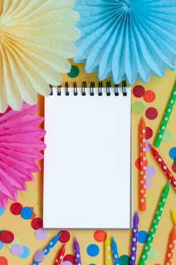 Boş kağıt boş, neşeli doğum günü renkli mumlar ve pastel sarısı arka planda kağıt vantilatörler..