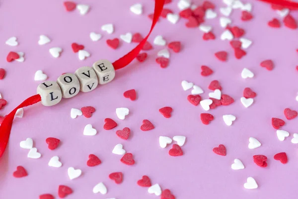 Κείμενο αγάπης σε κόκκινη κορδέλα σε ξύλινους κύβους σε ροζ φόντο με κόκκινες και λευκές καρδιές. Ημέρα του Αγίου Βαλεντίνου έννοια — Φωτογραφία Αρχείου