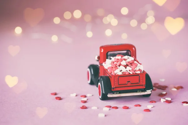 Miniature red car with a present box on the roof with red hearts on a pink background. Toned image. — 스톡 사진