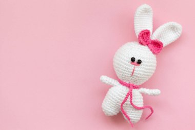 Pembe arka planda örülmüş küçük bir oyuncak tavşan. Düz yatış, üst görünüm