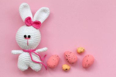 Pembe arka planda paskalya yumurtaları olan küçük bir oyuncak tavşan. Düz yerde, üst tarafta. Paskalya konsepti.